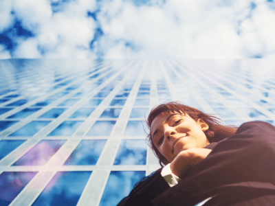 businesswoman looking down at camera in front of glass skyscraper