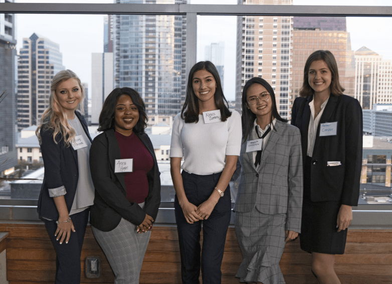 Five young women posing for photo at a UCREW event with buildings in background