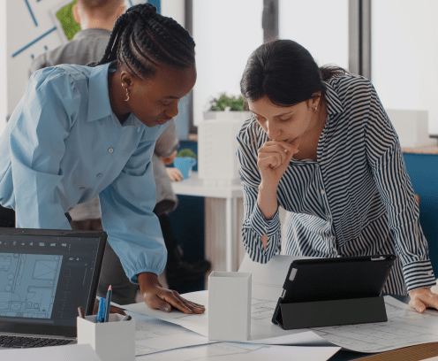 Close up of diverse women analyzing blueprints plan with digital tablet, doing teamwork for project. Architects working on construction layout and structure for urban development.