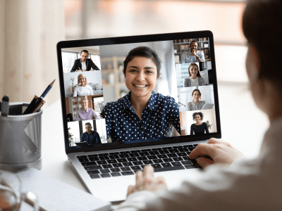 Woman sit at desk looking at computer screen where collage of diverse people webcam view. Indian ethnicity young woman lead video call distant chat, group of different mates using videoconference app